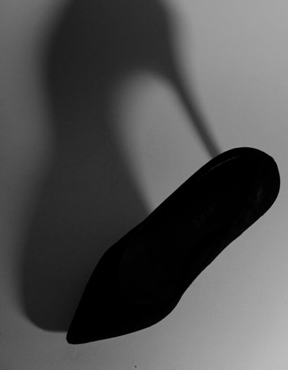 Monochrome photo of a black stiletto shoe casting a striking shadow on a plain background.