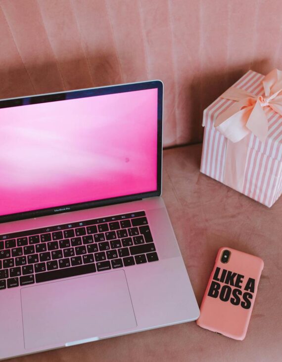 A modern workspace featuring a pink-themed laptop, a gift box, and a phone on a pink sofa.