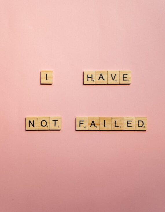 Wooden letter tiles form an inspirational quote on a pink background for motivation and design.